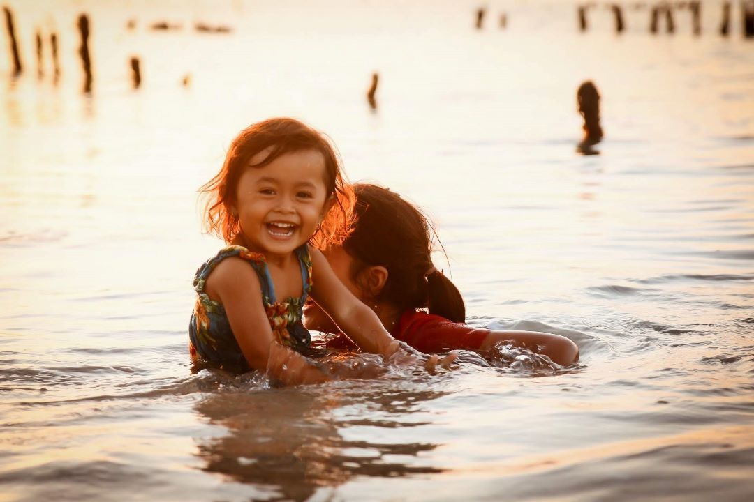 Niña bañándose en el agua mirando hacia a la cámara sonriendo en un atardecer